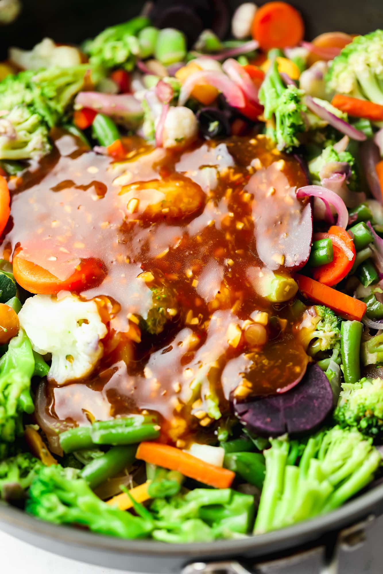 stir fry sauce on top of vegetables cooking in a black skillet.