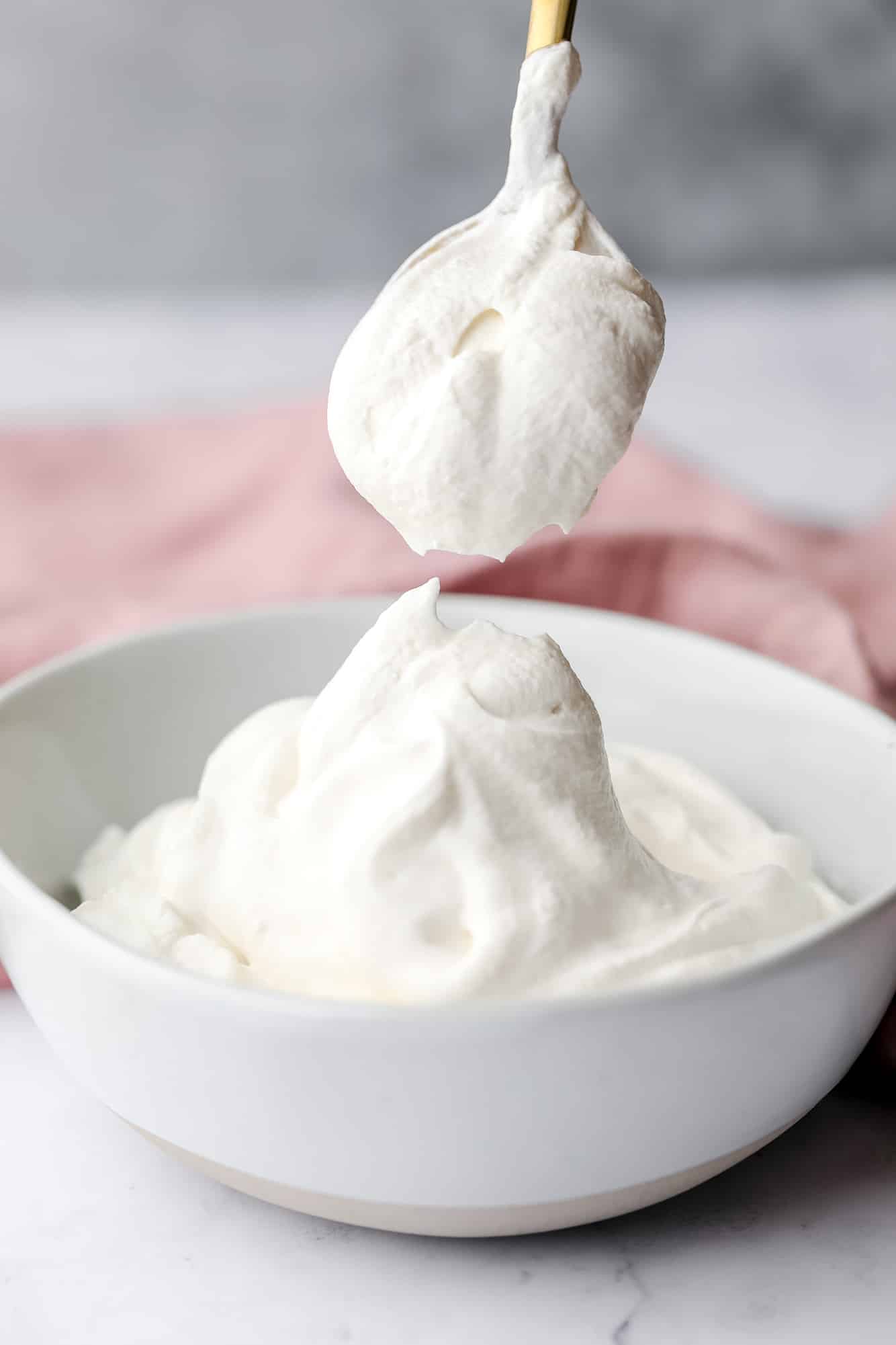 a spoon scooping a dollop of vegan whipped cream out of a white bowl.