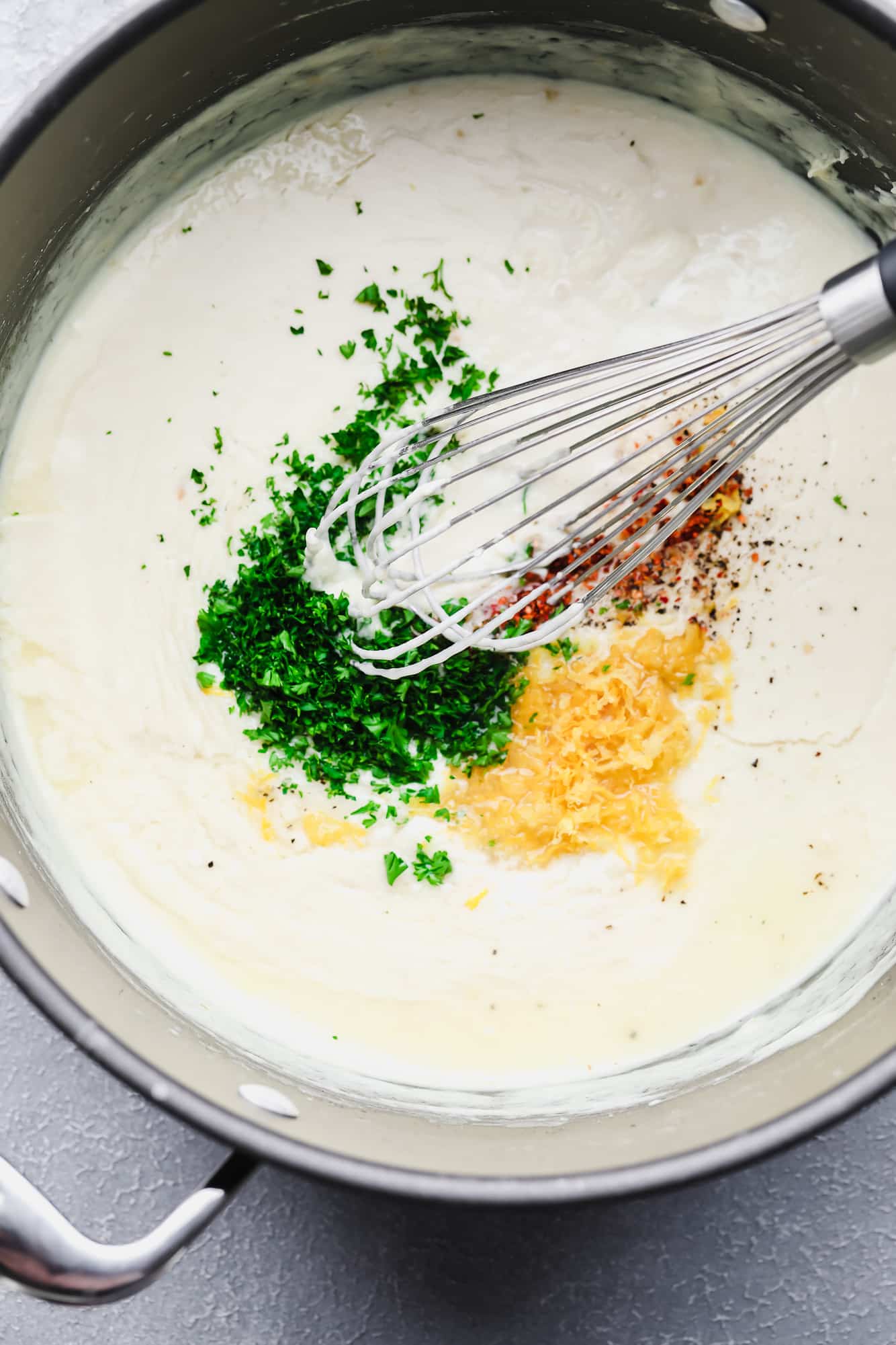 whisking lemon zest, parsley, and red pepper flakes into a white cream sauce in a pot.