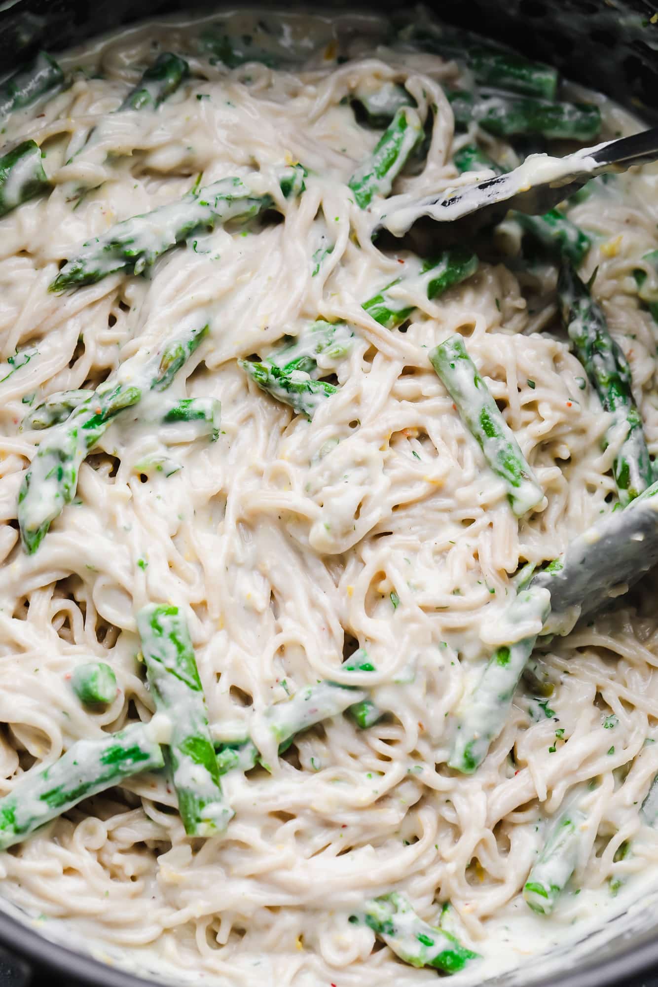 tossing lemon asparagus pasta with tongs in a large black pot.