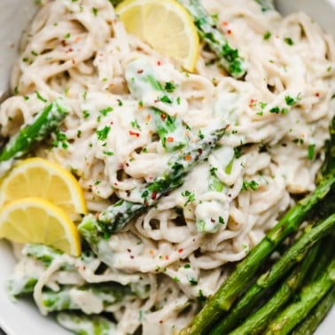 close up on lemon asparagus pasta topped with cooked asparagus and lemon slices in a white bowl.