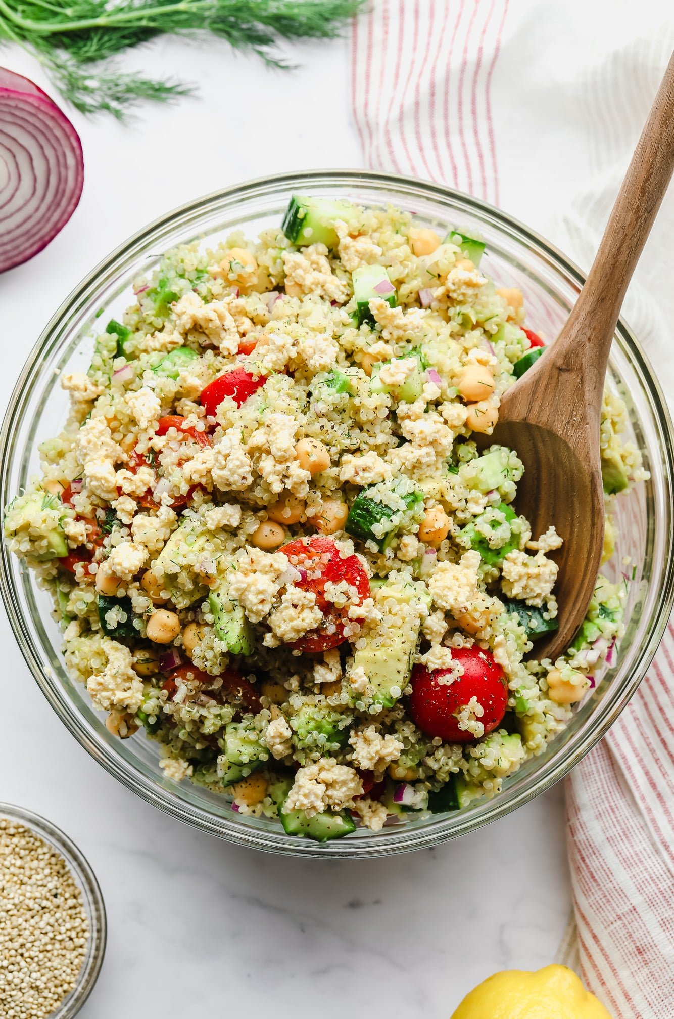 stirring a quinoa salad with chickpeas with a wooden spoon in a large glass bowl.