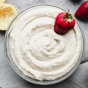looking down on a bowl filled with creamy white mixture and strawberries, grey background