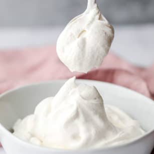 a spoon scooping a dollop of vegan whipped cream out of a white bowl.