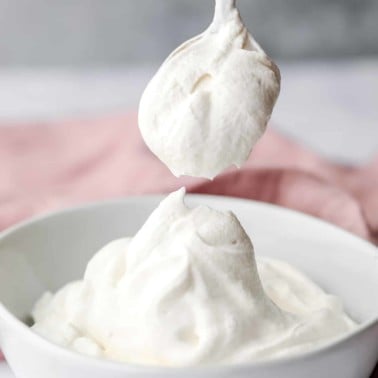 a spoon scooping a dollop of vegan whipped cream out of a white bowl.