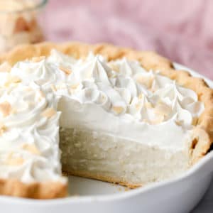 vegan coconut cream pie in a white pie plate with a slice removed.