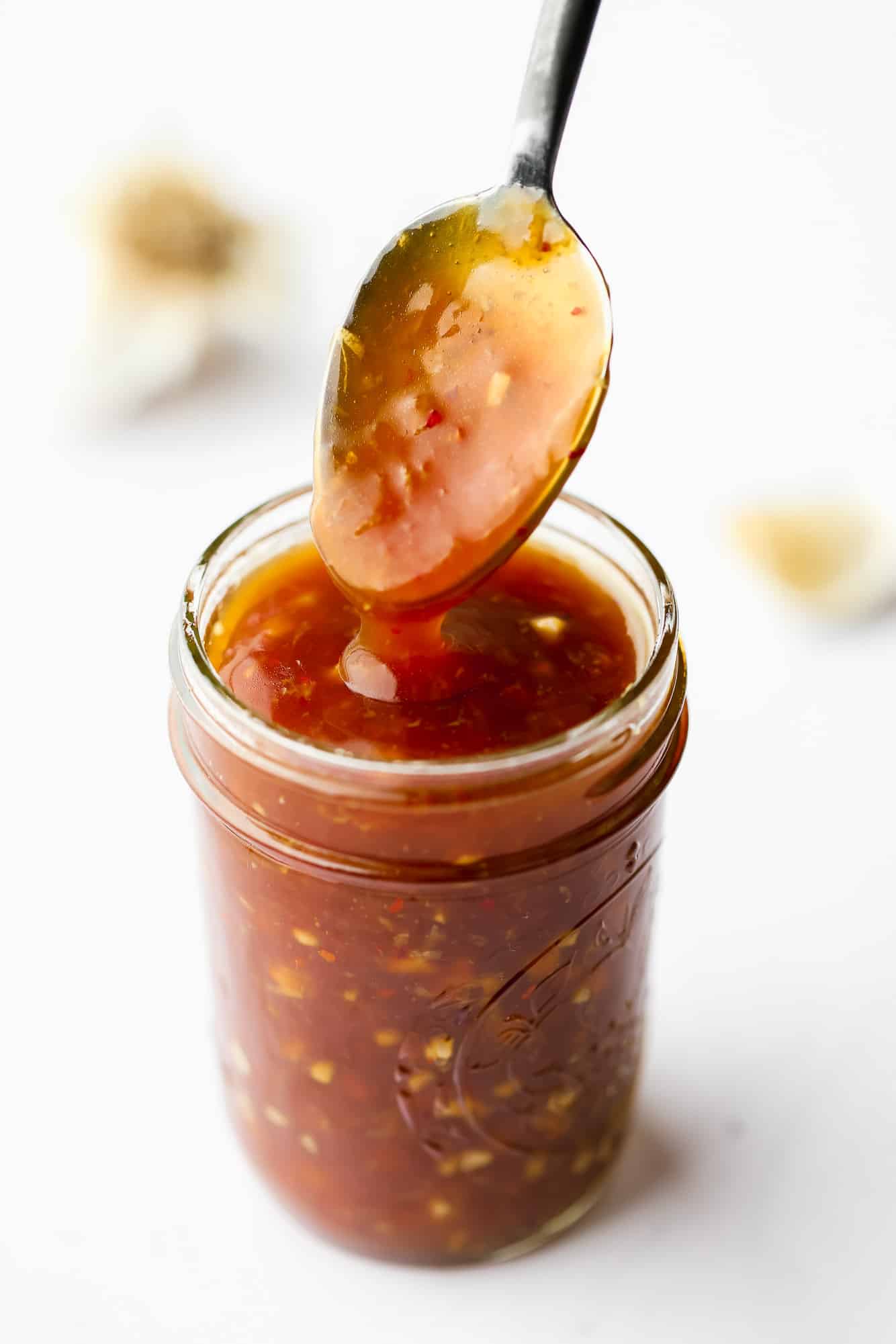 a sauce-covered spoon coming out of a jar of stir fry sauce.