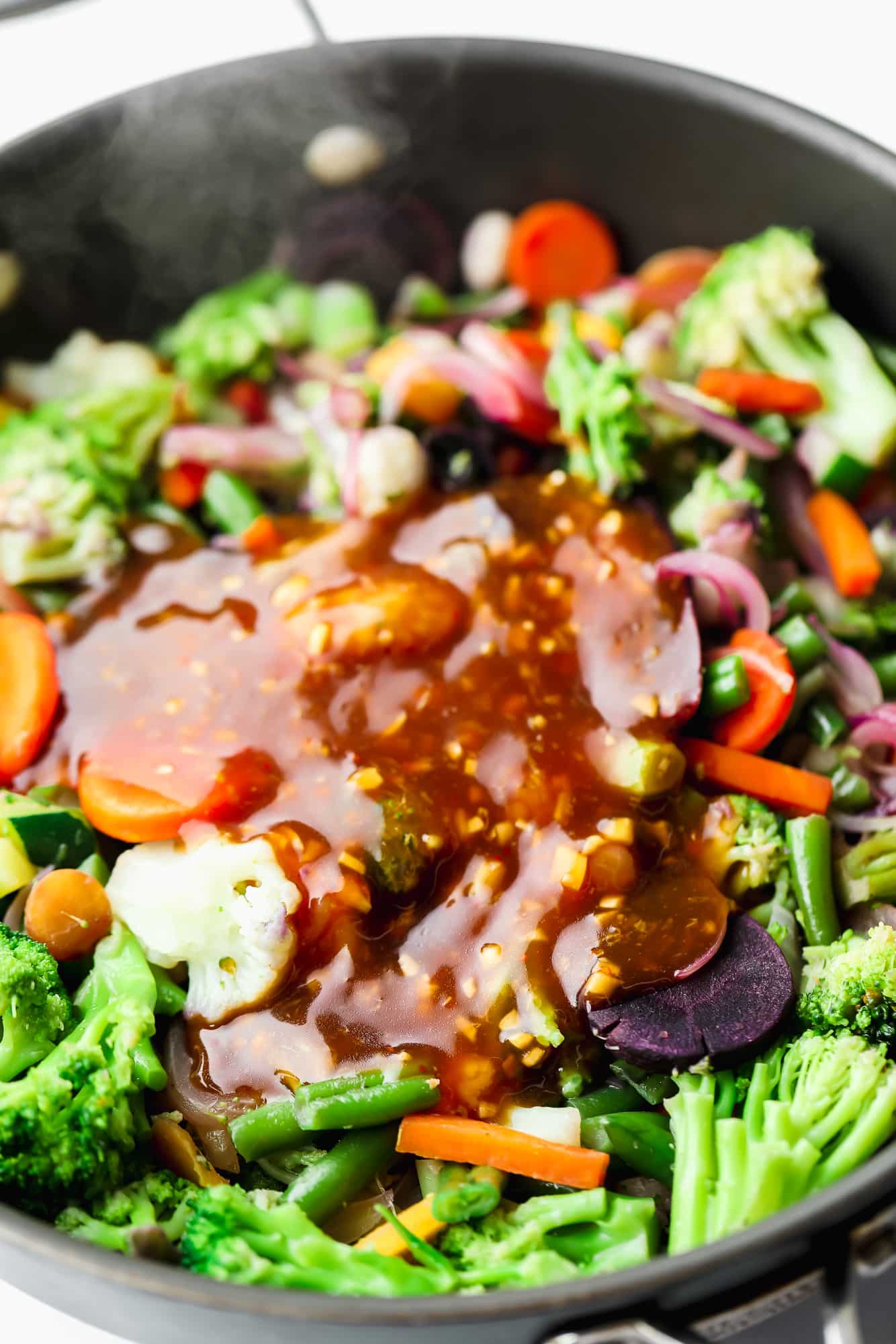 stir fry sauce on top of vegetables cooking in a black skillet.