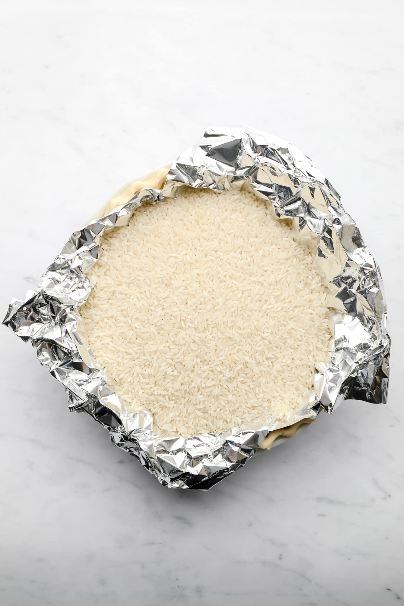 pie crust being baked in a pie plate with a layer of tinfoil and white rice on top.