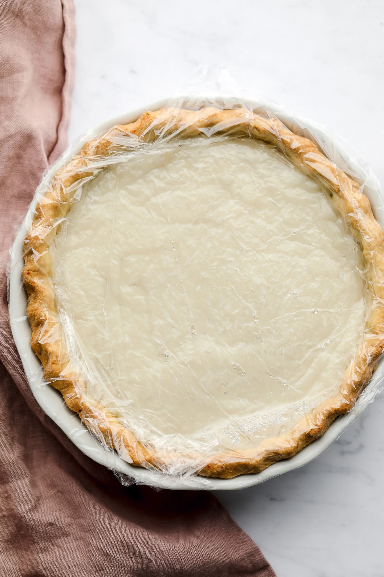 coconut custard in a pie covered with a layer of plastic wrap.