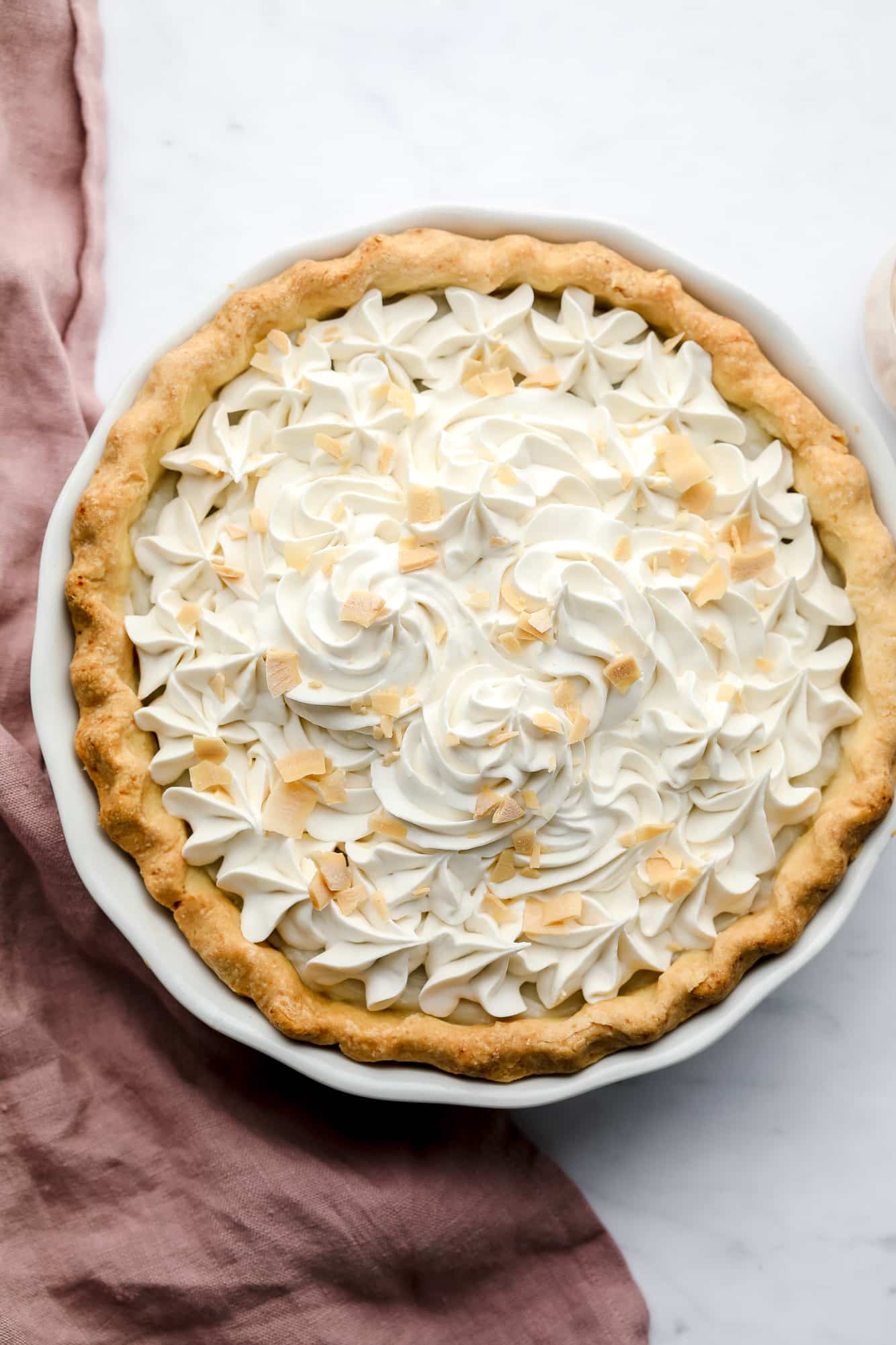 baked vegan coconut cream pie with whipped cream and toasted coconut shreds on top.