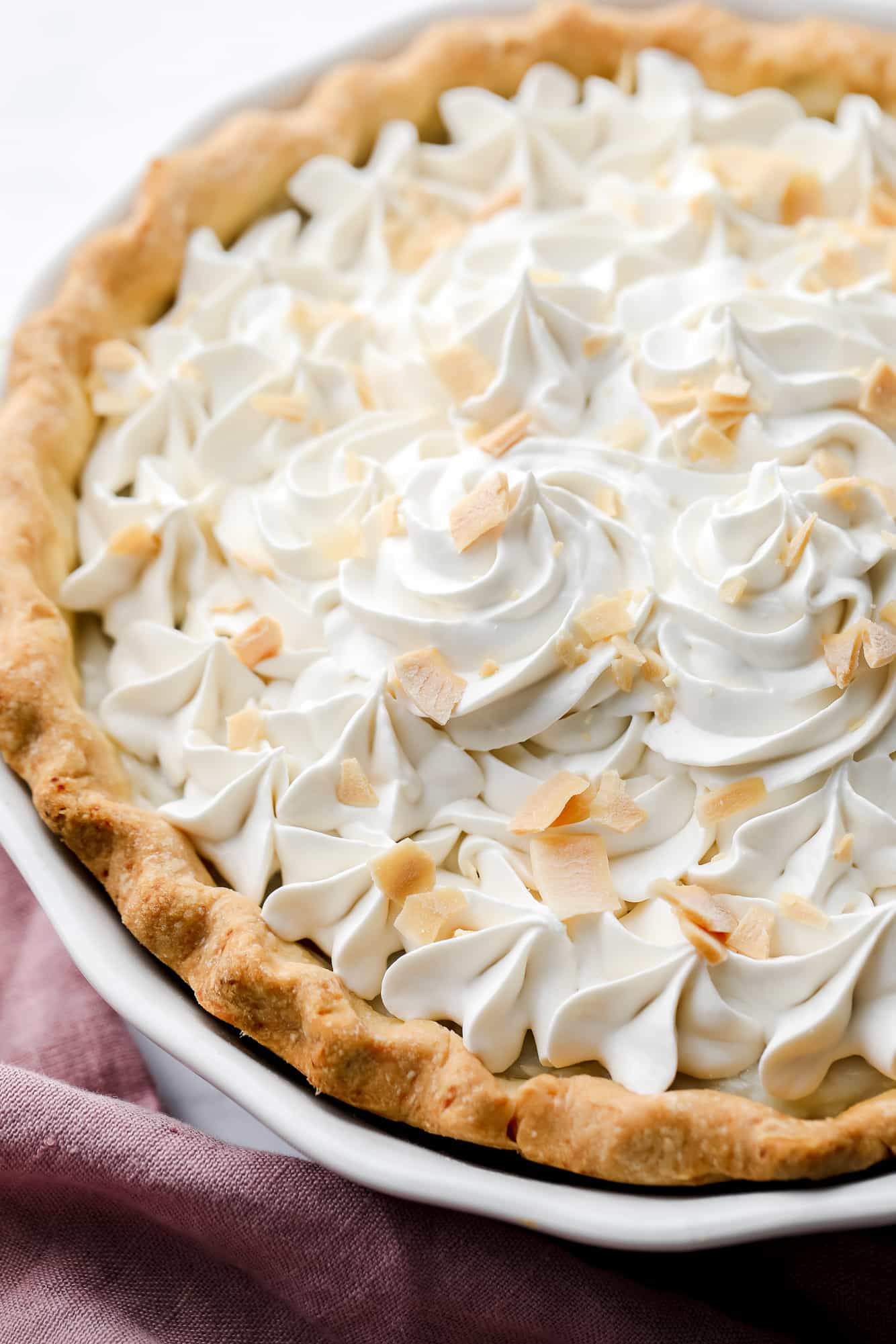 close up on a vegan coconut cream pie with whipped cream and coconut shreds on top.