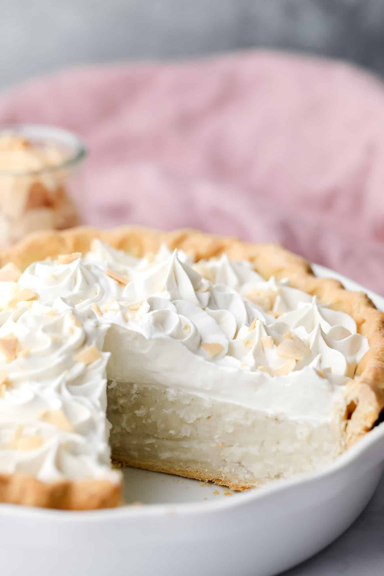 vegan coconut cream pie in a white pie plate with a slice removed.