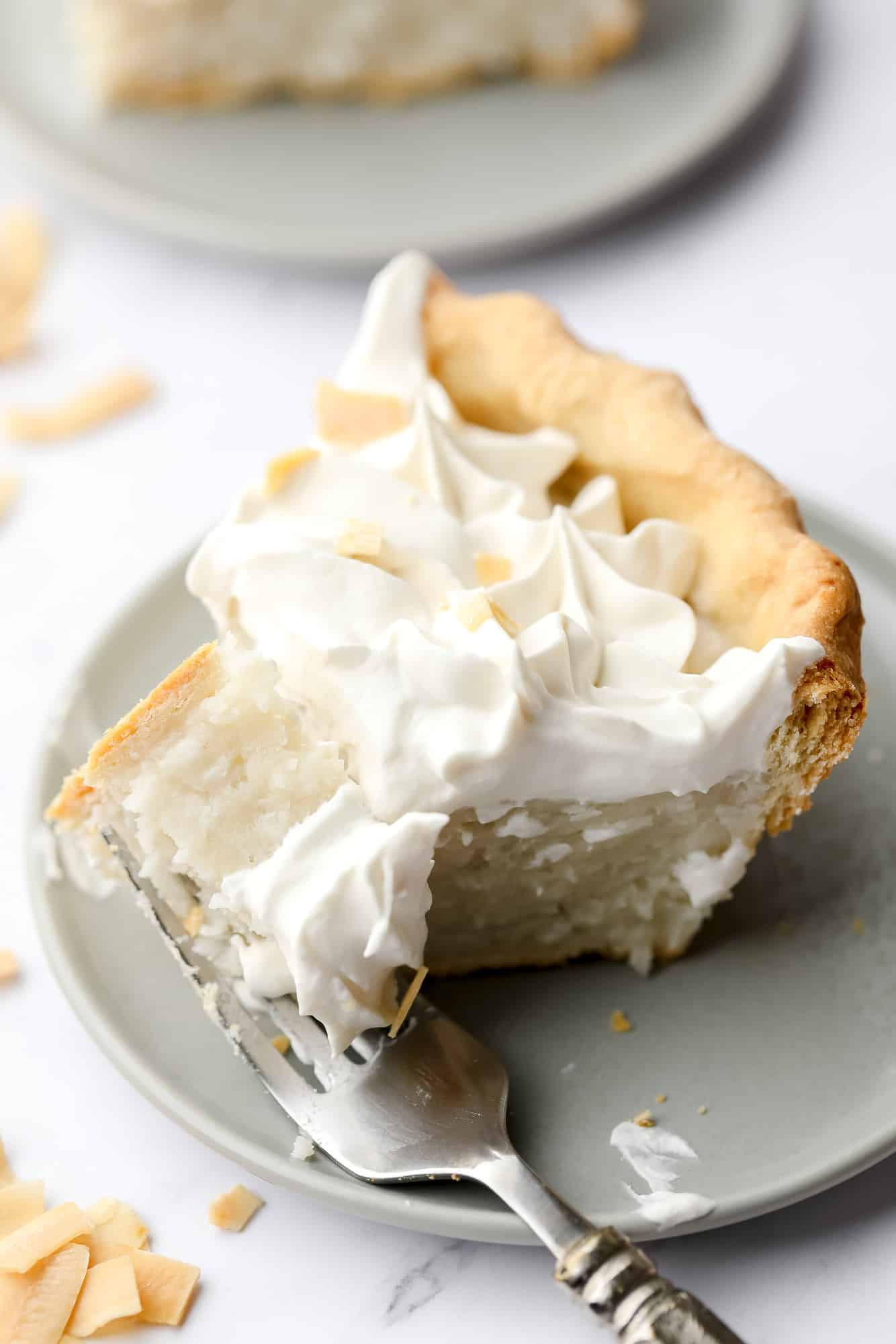 a fork taking a bite out of a slice of vegan coconut cream pie on a plate.