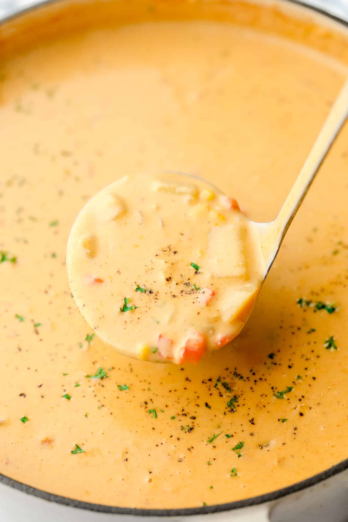 a ladle scooping vegan corn chowder out of a pot of soup.