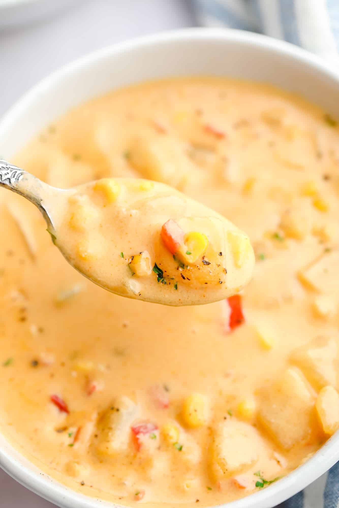 close up on a spoon full of vegan corn chowder with a bowl of soup in the background.