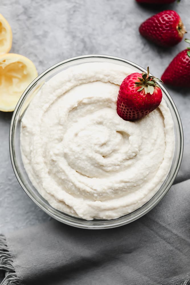 looking down on a bowl filled with creamy white mixture and strawberries, grey background