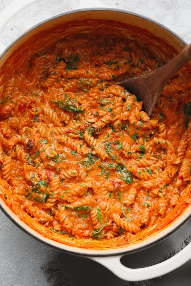 a wood spoon stirring vegan tomato sauce-covered pasta in a large white pot.