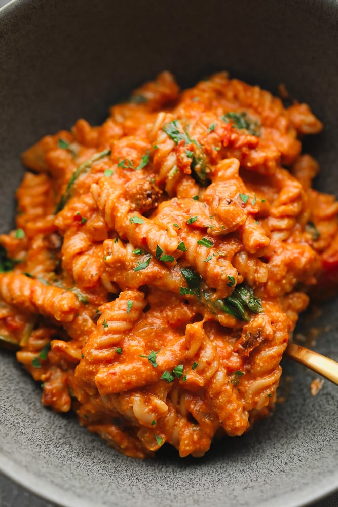 close up on vegan tomato sauce-covered pasta in a grey bowl.