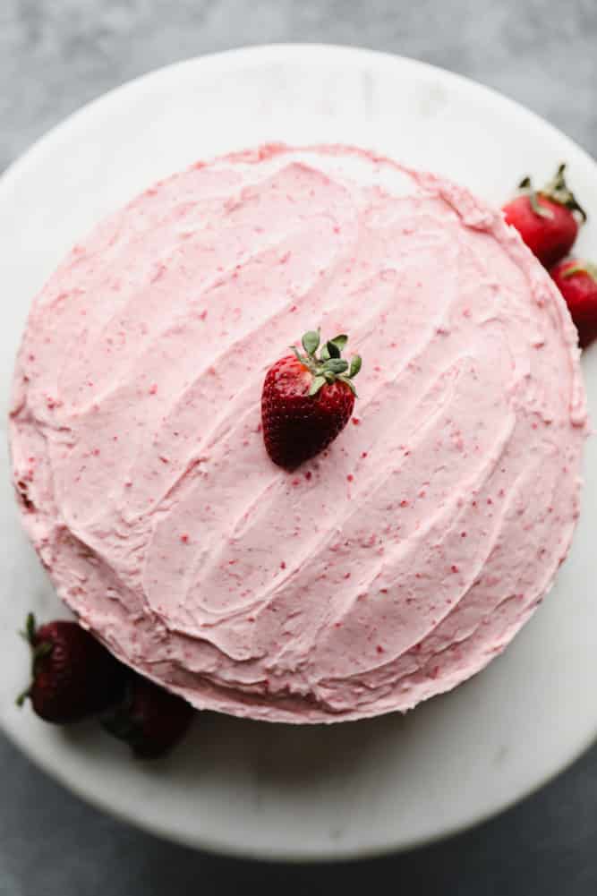frosted pink cake with strawberries, on marble cake stand