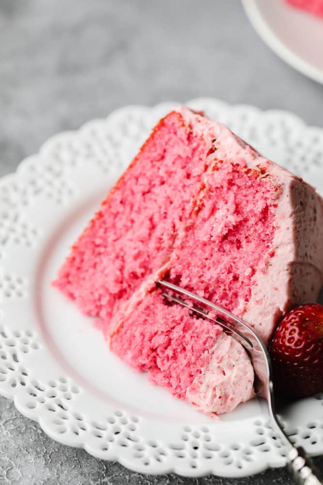 fork cutting into piece of vegan strawberry cake on white plate