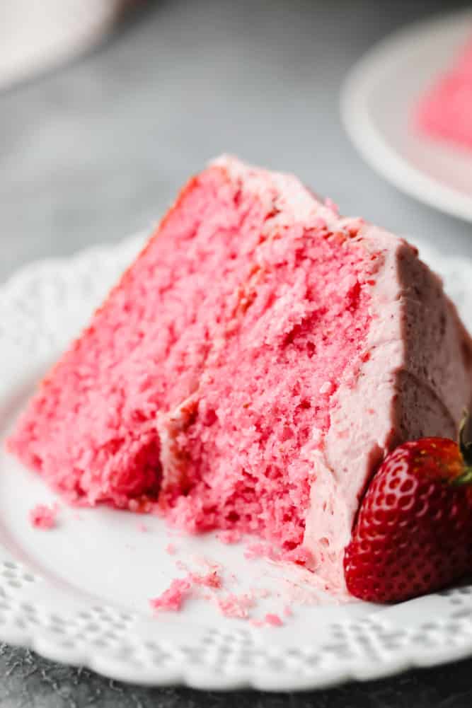 a bite taken from a piece of pink cake with strawberry on the side of the plate