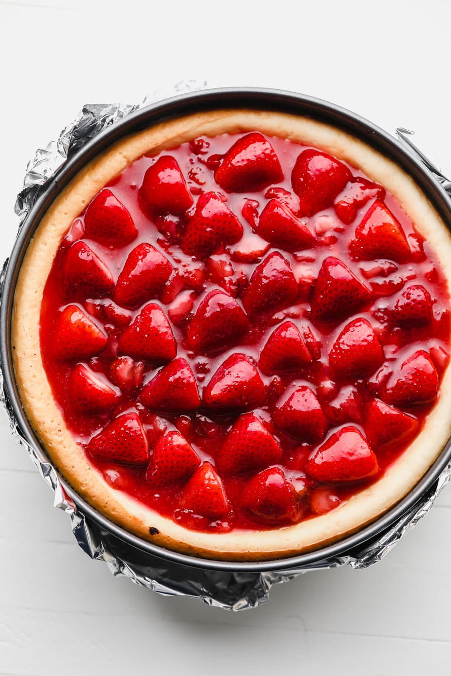 vegan cheesecake topped with strawberry sauce in a springform pan.
