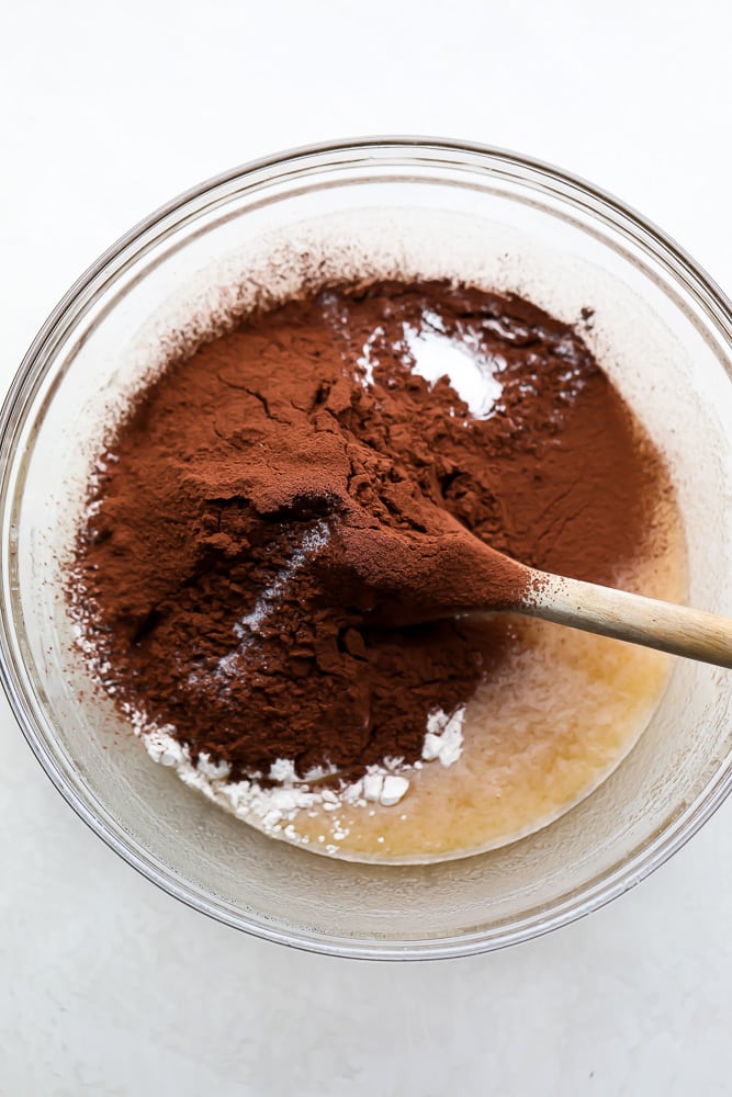 cocoa powder added to clear bowl with wet ingredients