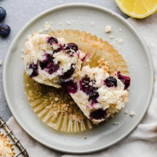 a gluten free blueberry muffin cut in half on a small white plate.