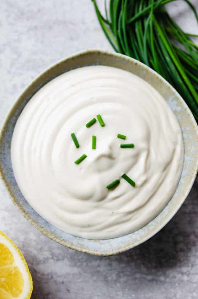 small speckled bowl of vegan sour cream with chives on top, grey background