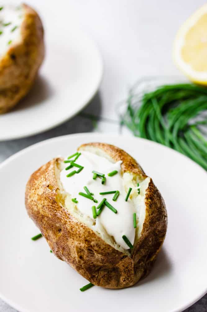 two baked potatoes with sour cream and chives, white background