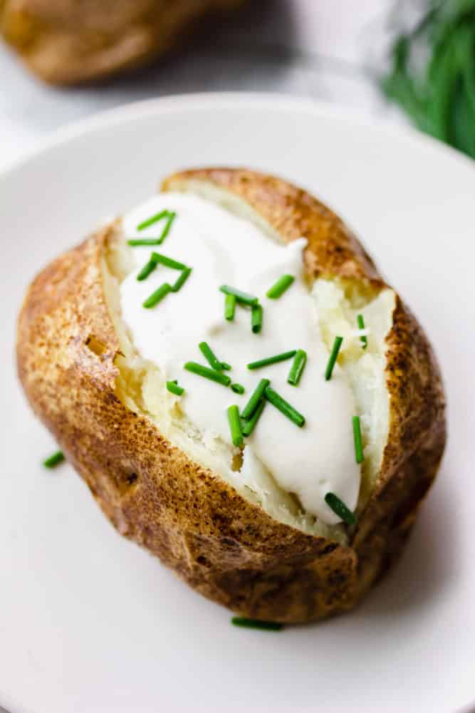 white plate with a baked potato, sour cream and chives