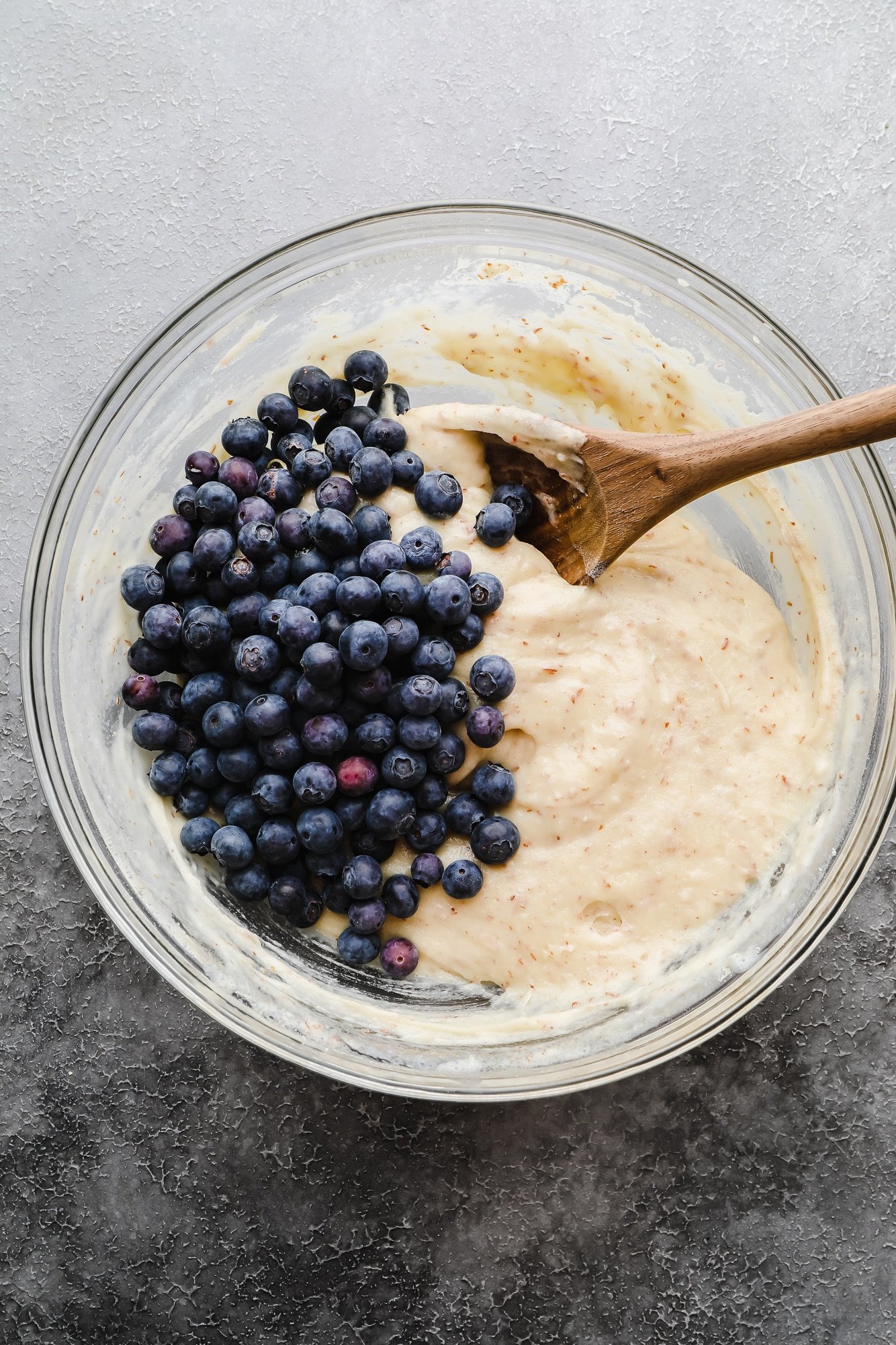 Folding fresh blueberries into muffin batter with a wooden spoon.