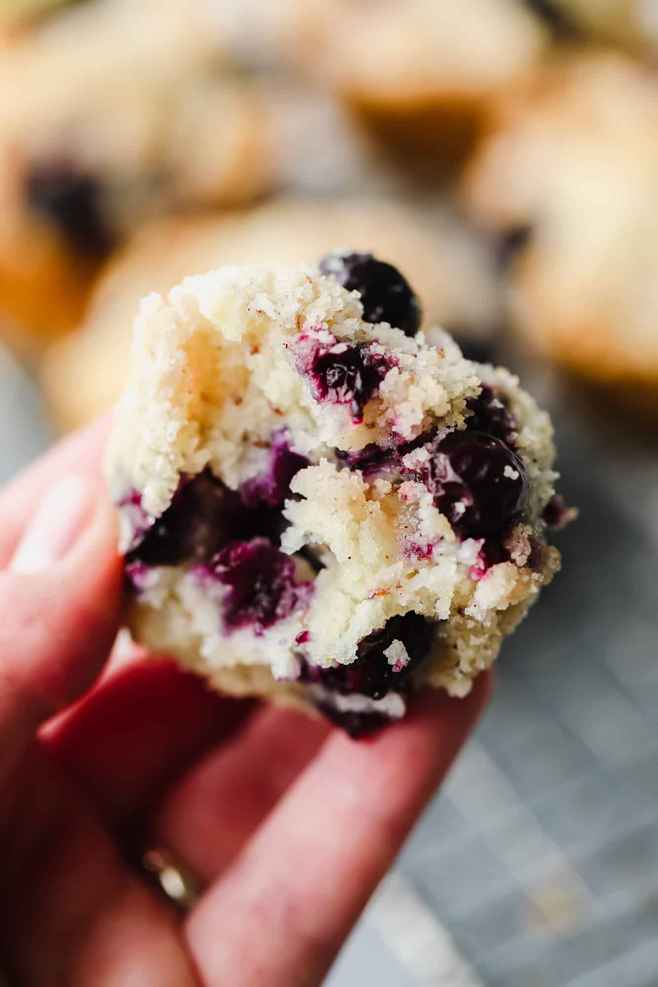 close up on a womans hand holding half of a gluten free blueberry muffin.