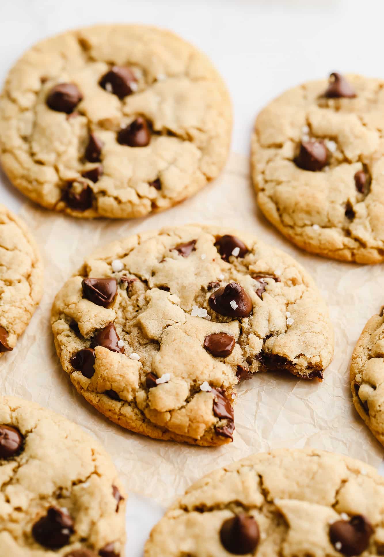 a chocolate chip cookie with sea salt on parchment paper with cookies all around it