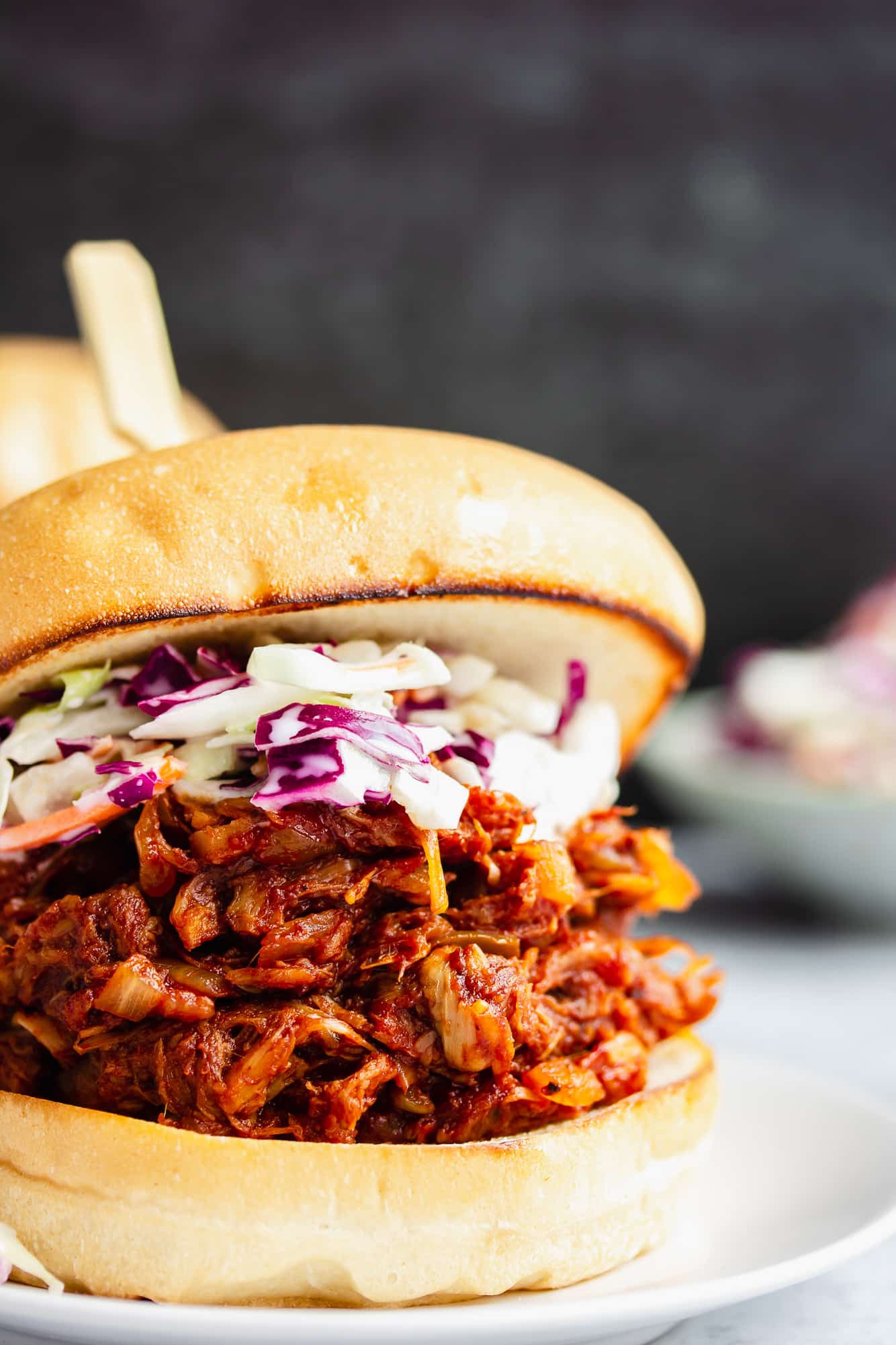 close up on a jackfruit pulled pork sandwich topped with coleslaw on a white plate.