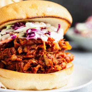 close up on a jackfruit pulled pork sandwich topped with coleslaw on a white plate.