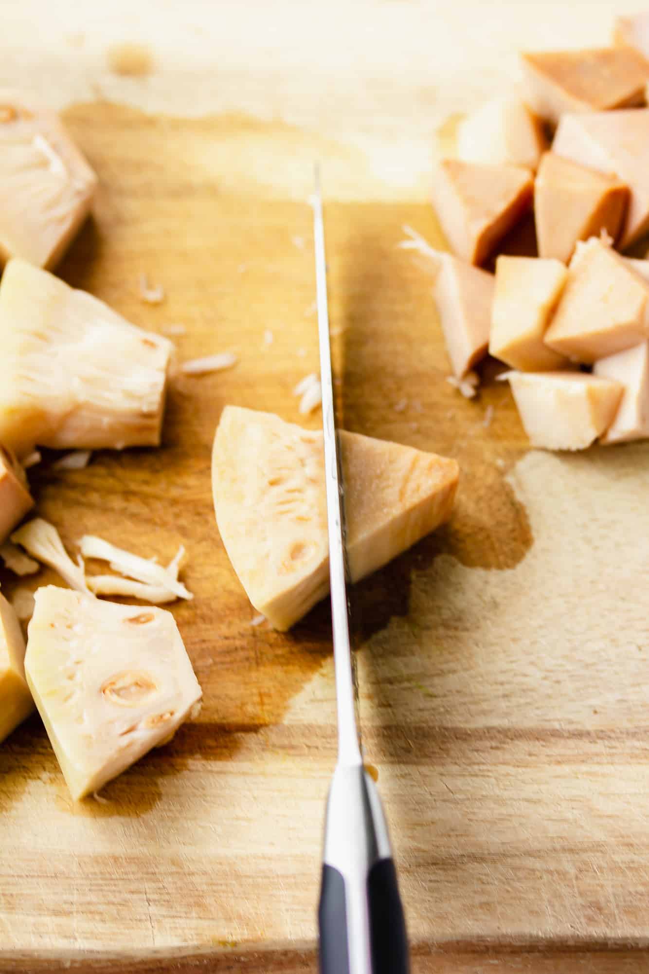 using a knife to cut young jackfruit on a wooden board.