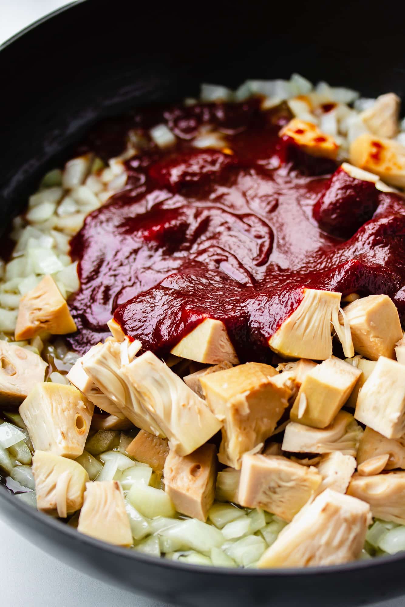 jackfruit cooking in a large black skillet with onion and barbecue sauce.