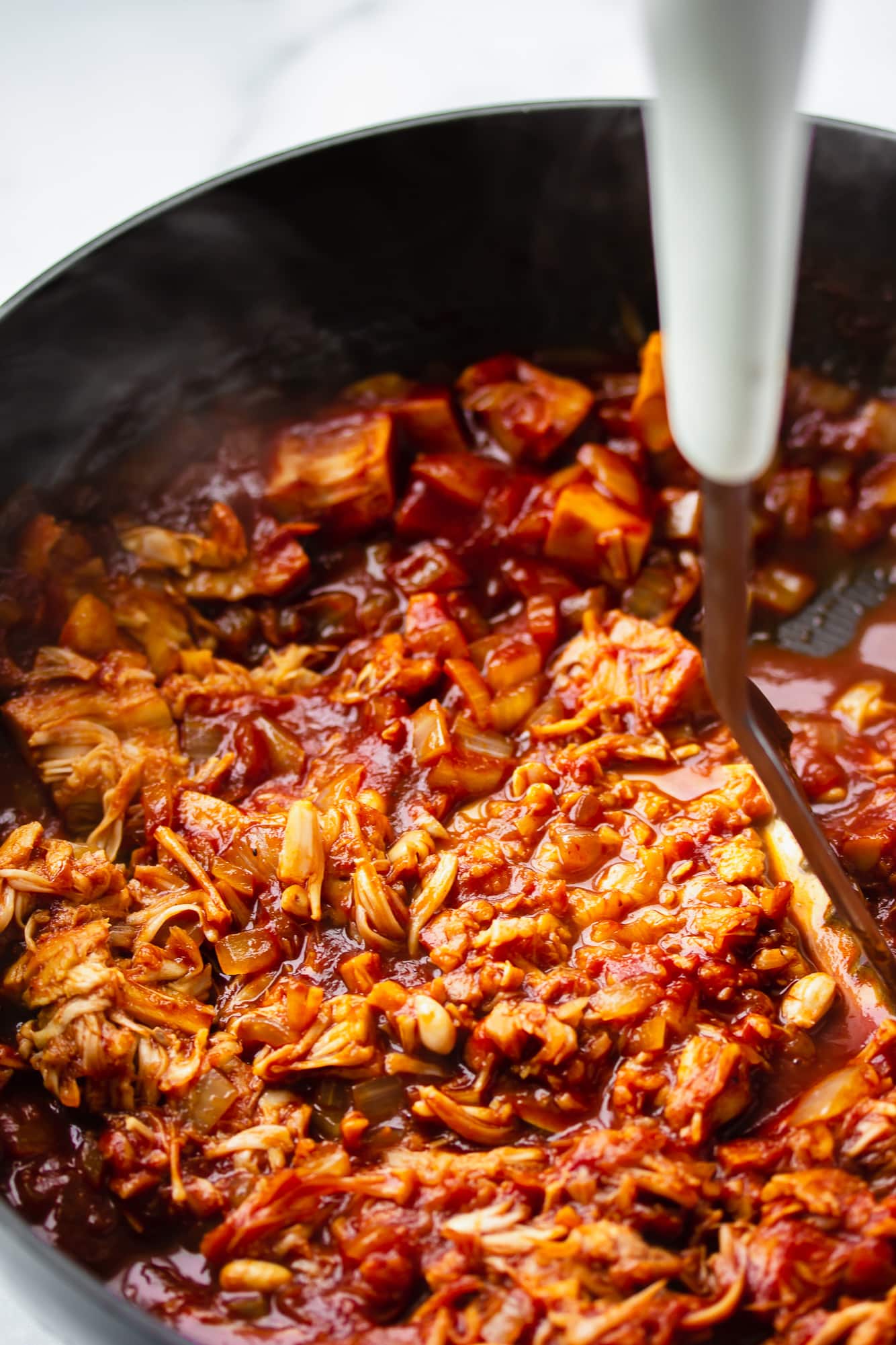 mashing vegan pulled jackfruit in a skillet with a potato masher.