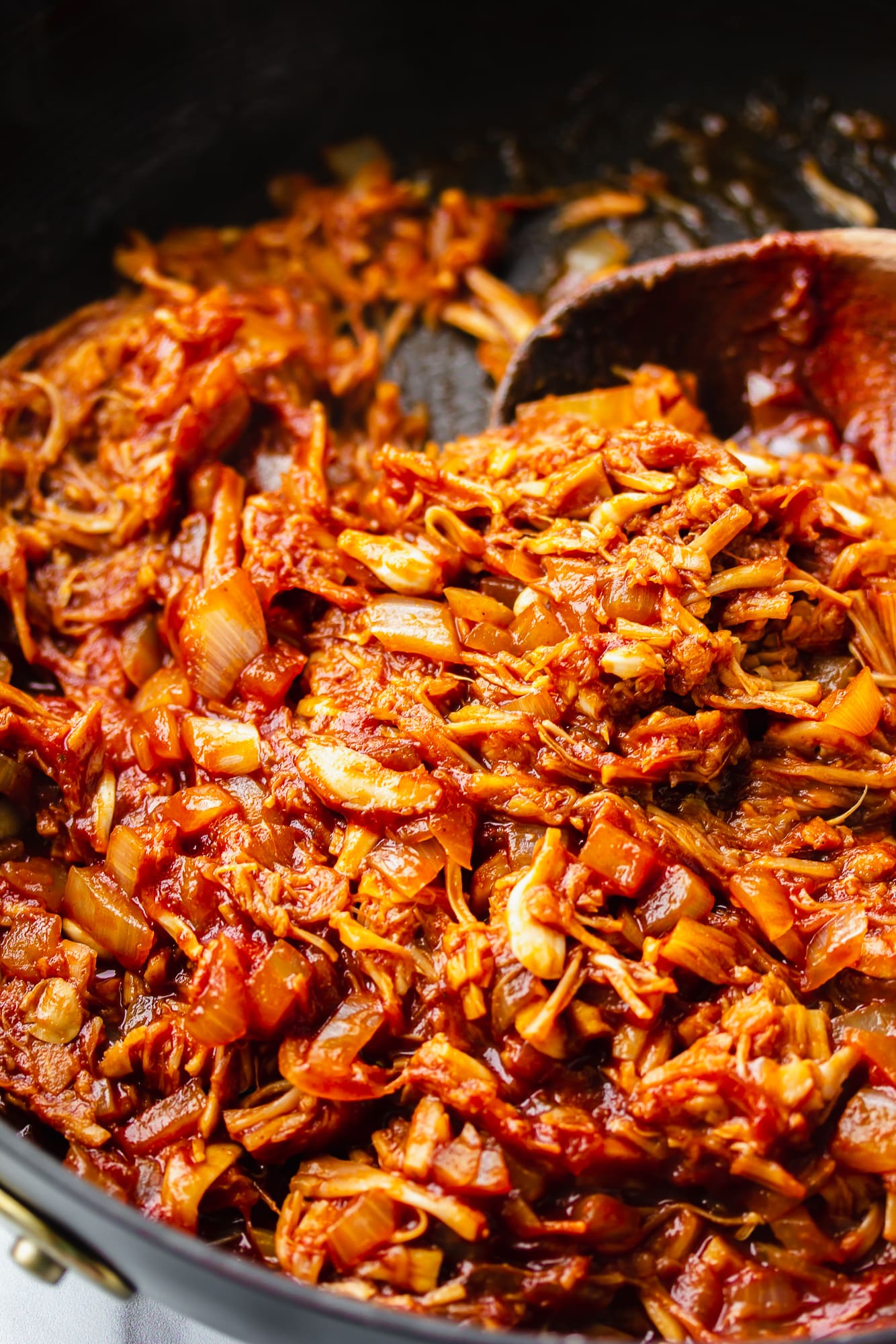 stirring jackfruit pulled pork with a wooden spoon in a skillet.