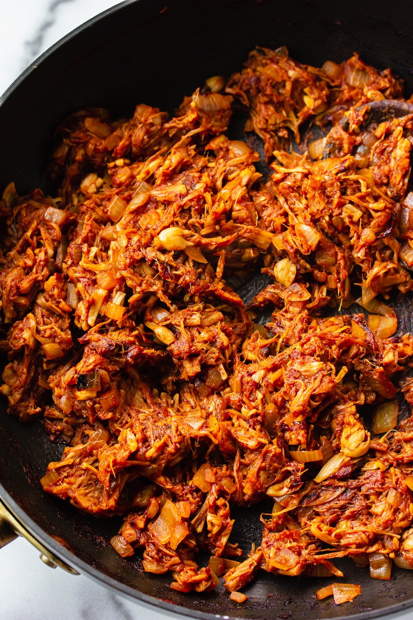 stirring jackfruit pulled pork with a wooden spoon in a skillet.