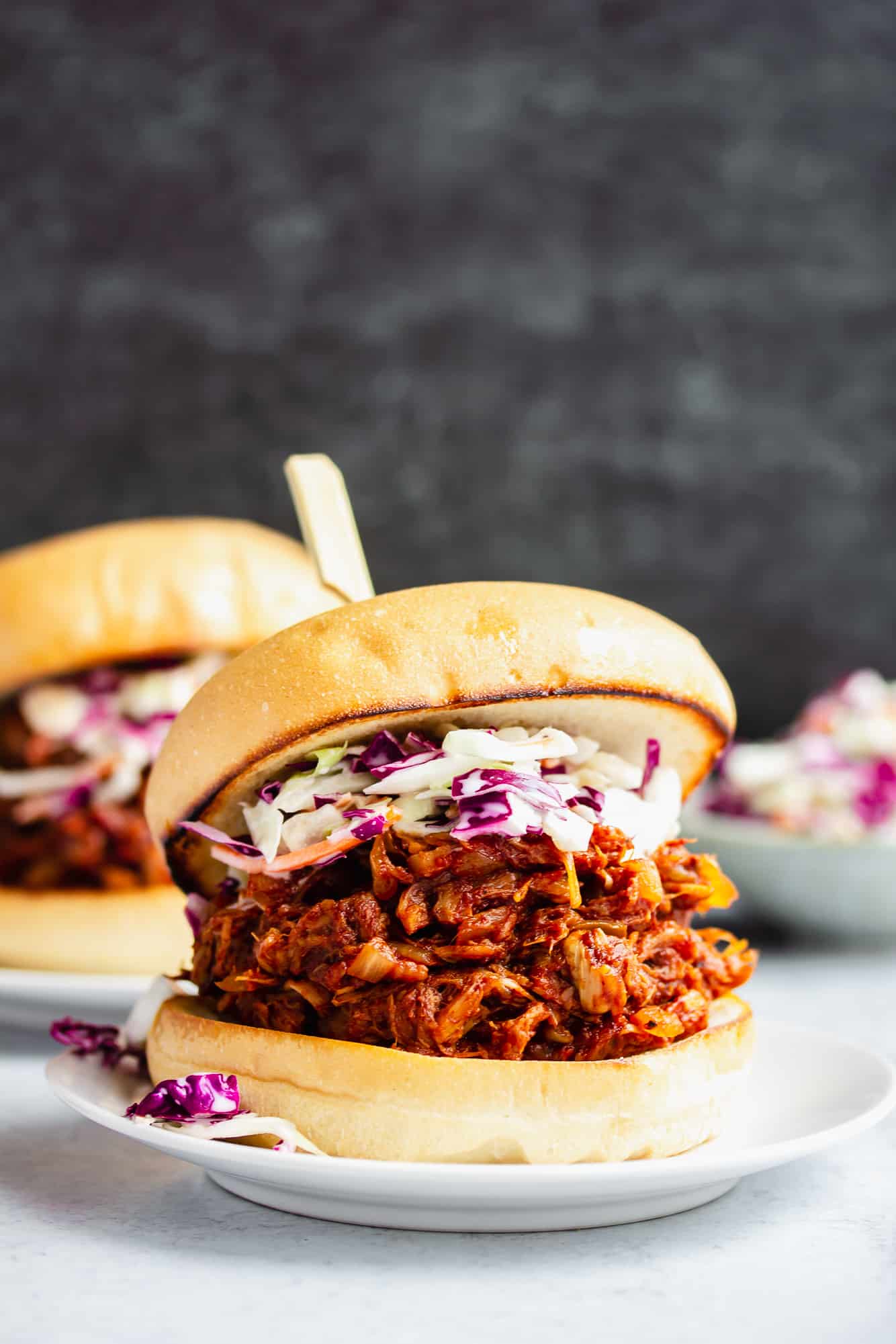 jackfruit pulled pork sandwich topped with coleslaw on a white plate.