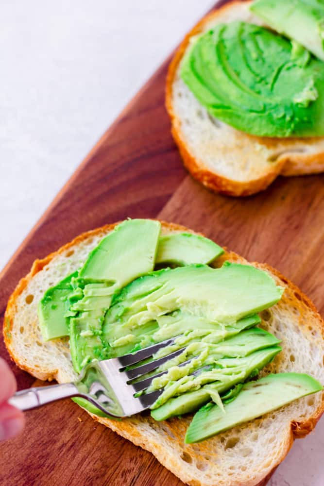 a fork mashing avocado on bread