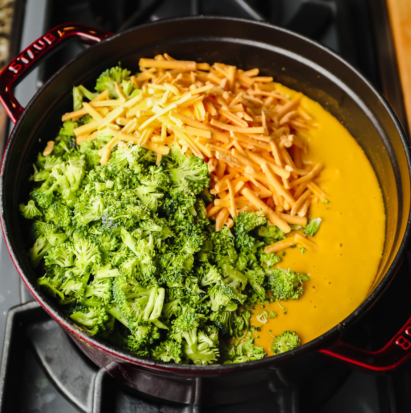 broccoli florets and shredded vegan cheese on top of a pot of broccoli cheddar soup in a large black pot.