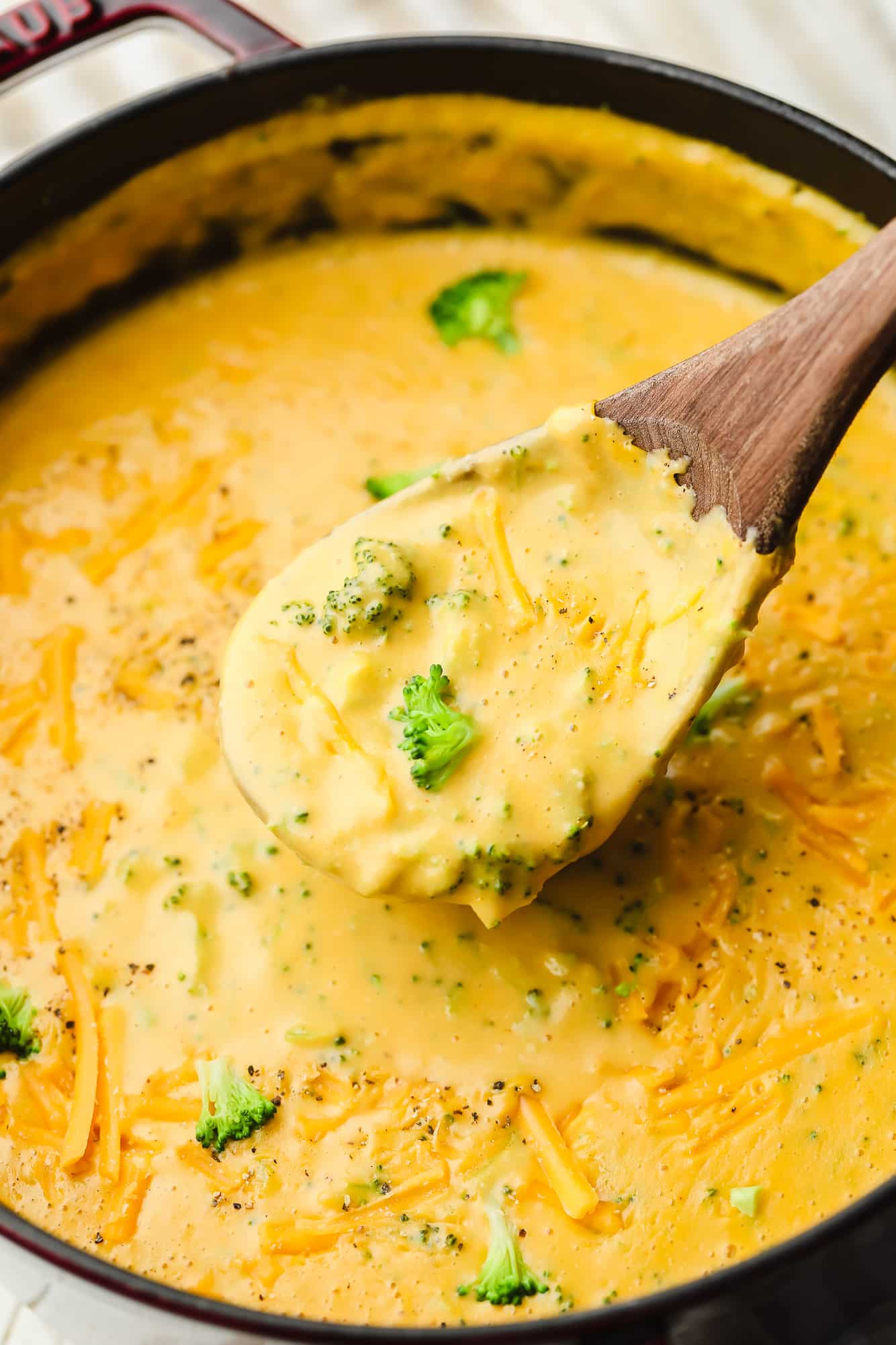 scooping up vegan broccoli cheddar soup with a wooden spoon.