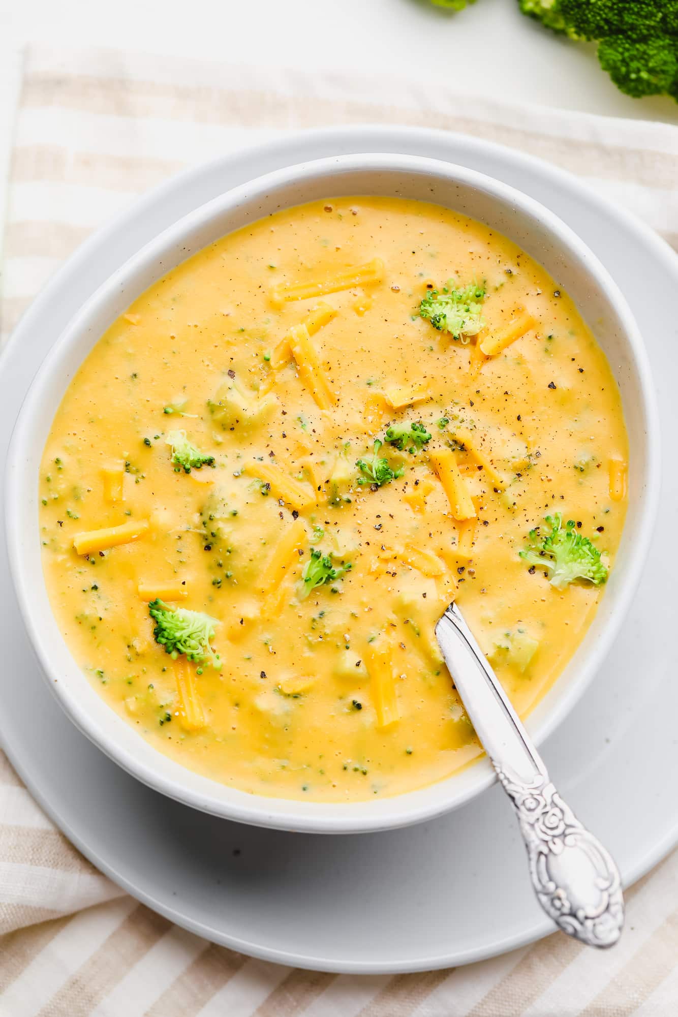 a white bowl filled with vegan broccoli cheddar soup and a spoon.