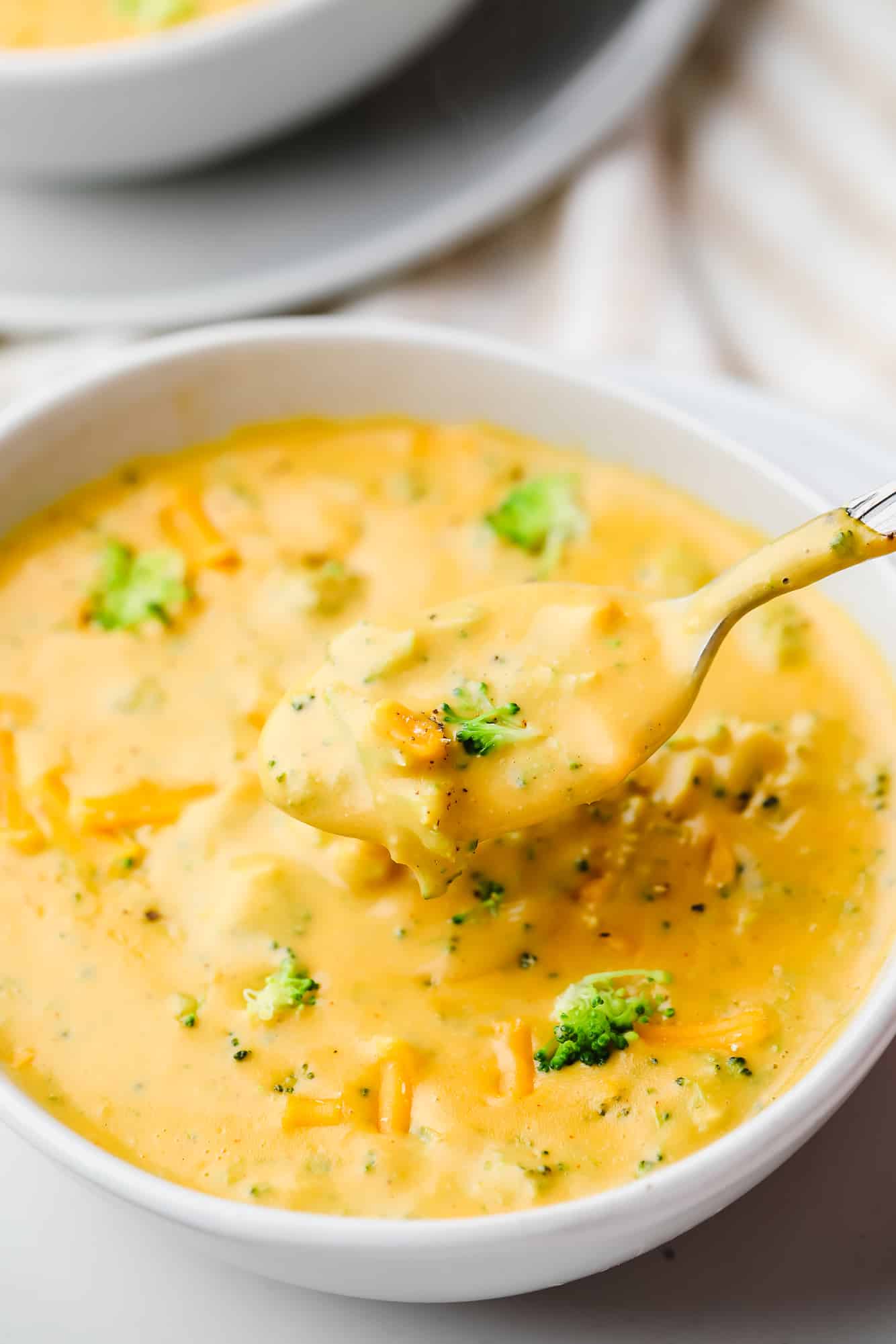 a spoon taking a scoop of broccoli cheddar soup out of a white bowl.