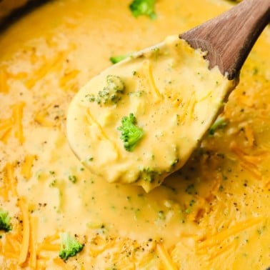 close up on a wooden spoon scooping vegan broccoli cheddar soup out of a pot.