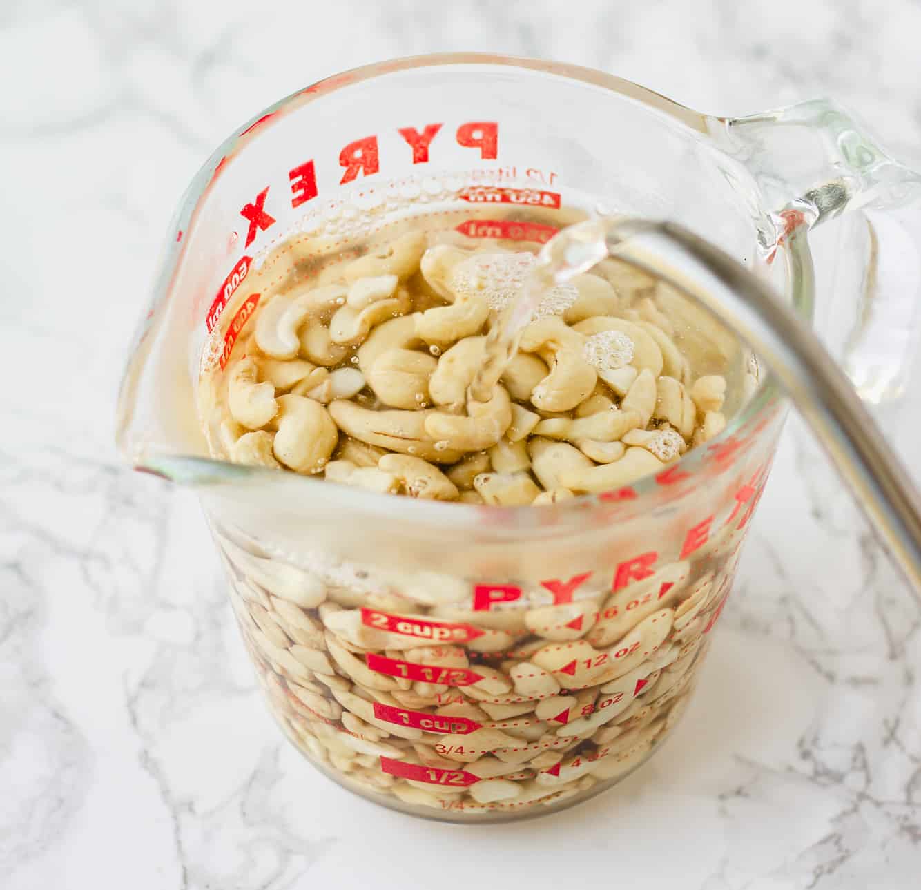 soaking cashews in hot water in a large glass measuring cup.